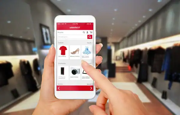 Une personne utilisant un smartphone pour faire du shopping en ligne avec l'application eMarket, dans un magasin moderne de vêtements et accessoires.